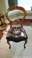 Front view of vintage wooden chair showing carved upper backrest and floral needlepoint upholstered seat.
