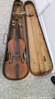 Vintage violin placed inside an open wooden case, showing overall condition of violin and lining of case.