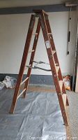Side view of six-foot wooden step ladder showing wooden beams, metal hinges, braces, and four steps on each side.