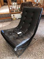 Angled view of black tufted leather chair on stainless steel sled base showing curved seat and overall condition