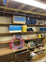 Shelf containing the blue and white Coleman cooler, yellow drink cooler, folded outdoor flag, and assorted boxes and games below.