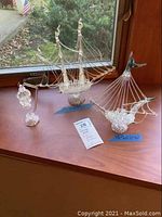 Wide view of two glass ships and hanging lantern placed on wooden surface near window showing all items in set.