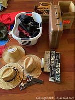 Overview image showing straw hats, metal suitcase, wooden hangers, tie and belt racks, laundry basket with umbrellas, duffel bags, and reusable bags on wood floor.