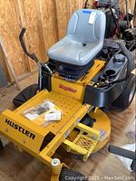 Front-side view of yellow Hustler Raptor zero-turn mower with grey vinyl seat and black deck housing
