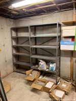 Two metal shelving units located in a basement corner; items on shelves and boxes on floor not included in the lot.