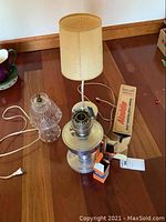 Wide shot of the oil lamp with glass globe, lamp shade, mantles, and boxes on wooden floor