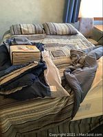 View of the bed made up with the quilt, comforter partially folded, two matching striped pillows, and the boxed flannel sheet set on top of the bed.