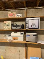 Overview photo showing all appliances on shelves: Sous Vide water oven in box, electric broiler, Waring 4-way mixer in box, Sunbeam sharpener box, Zojirushi Home Bakery bread maker on lower shelf