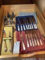 Full drawer layout showing 16 knives with pearl handles, 4 salt and pepper shakers, and a serving knife and fork in a yellow cloth sleeve.
