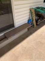 Stone slab placed horizontally on a concrete patio against a light-colored siding wall, showing overall rectangle shape and brown color.