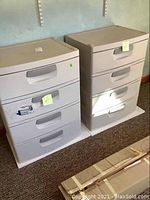Two beige/light gray Sterilite plastic 4-drawer storage units side by side on carpeted floor, showing front drawer faces and handles.