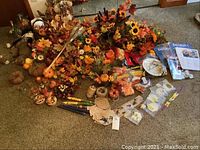 Wide view of the lot showing faux florals, scarecrows, pumpkins, candles, twine and other autumn decorations displayed on carpeted floor.