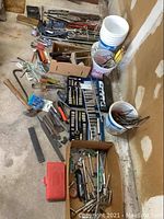 Wide view of assorted hand tools arranged on floor and in buckets and boxes showing various hand tools including hammers, screwdrivers, wrenches, chisels, and ratchets