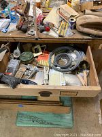 Wooden workbench drawer open showing assorted hand tools, brushes, metal wires, small hardware, and utility items inside the drawer and on the benchtop.