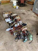 Full view of various tools, flashlights, hand saws, hammers, and power tools scattered on garage floor.