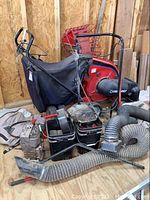 Full view of red Troy-Bilt chipper vac with attached black collection bag and loose engine parts on floor.