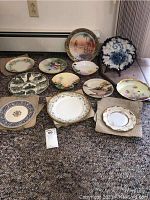 Overview of all 12 vintage plates arranged on floor, showing variety of styles and colors.