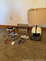Overview photo of vintage toys and football helmet lamp on carpeted floor against beige wall.