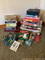 Photo showing stack of vintage board games and two Walt Disney hand puppets on carpet. Various game titles visible including Boggle and Can't Stop.