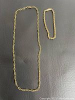 Chain necklace and rope-link bracelet laid flat on black surface