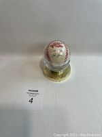 Baseball in clear plastic display sphere with brass-tone base and MaxSold lot tag #4