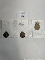 Three watch fobs laid flat: two circular dark metal pieces with 1908 presidential election inscriptions and one shield-shaped badge for Chicago Centennial Jubilee.