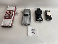 Four collectible model cars displayed in a row on a white surface.