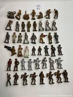 Overall lot view showing about 50 vintage lead army men figures arranged in rows on a white surface