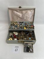 Large open jewelry box showing two tiers filled with assorted costume jewelry including brooches, pins, earrings, necklaces, and watches.