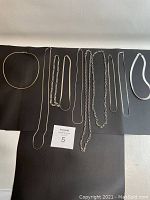 Full lot view of 7 sterling silver necklaces on black background showing varying chain styles and lengths.