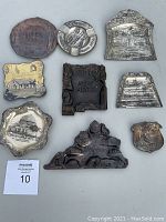 Nine assorted metal ashtrays arranged on flat surface showing various embossed and engraved designs including Washington D.C., New Mexico, and Virginia landmarks.
