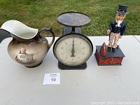 Overview of the three items side by side on a table outdoors: ceramic pitcher, metal scale, and Uncle Sam bank.