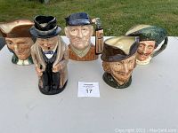 Lot of five Royal Doulton character mugs displayed outdoors on a white table. Each mug features detailed human faces with distinctive hats and expression. All mugs show some signs of use.