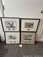 Four framed vintage duck stamp prints with two duck stamps each, signed by artist, arranged on floor against white wall.