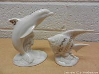 Photo of two Lenox figurines: a dolphin jumping on waves and a fish on base, both white porcelain with gold detailing.