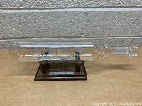 Side view of the glass ship inside bottle mounted on a wooden stand with silver label.