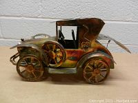 Front and side view of a vintage metal car music box with detailed wheels and side-mounted spare tire, showing the trunk in closed position.