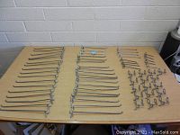 Top-down view showing multiple organized rows of different lengths and types of pegboard hooks on a table against a white brick wall.