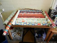 Photo of multiple rolls of Christmas wrapping paper laid out on a table showing a variety of holiday-themed patterns and colors.