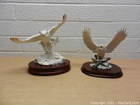 Both owl figurines together on a table against a white brick wall, showing their relative size and detail.