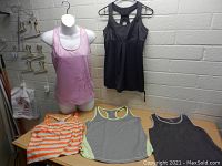 Lot of 5 women's activewear tops on a table and mannequin, showing variety of styles and colors.