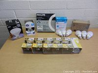 Front view of assorted new light bulbs on table showing a variety of brands, box packaging, and loose bulbs.