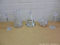 Front view of six clear crystal collectibles arranged in a row against a white brick wall, showing detail and design of each piece.