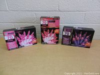 Three unopened boxes of pink and purple C7 Christmas string lights placed on a table against a brick wall background.