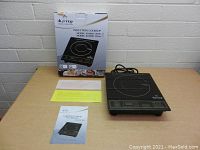 Image shows the induction cooktop, original box, user manual, and paperwork on a table against a brick wall.