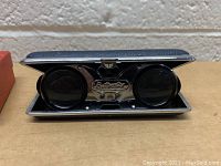 Opened binoculars showing eyepieces, lenses, and metal plate engraved with brand name.