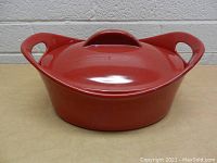Front view of red ceramic pot with lid and two loop handles on sides.