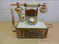 Front view of vintage rotary phone showing the rotary dial, handset, and ornate metal decorations.