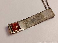 Close-up front view of amber and sterling silver rectangular pendant on chain showing amber inset and tarnished silver surface.