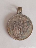 Front view of antique silver coin with visible engravings and attached soldered loop for pendant use.